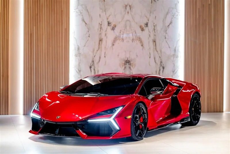 A sleek red Lamborghini Revuelto with black accents is parked indoors against a marble and wooden panel backdrop, epitomizing the elegance of 2024's automotive design.