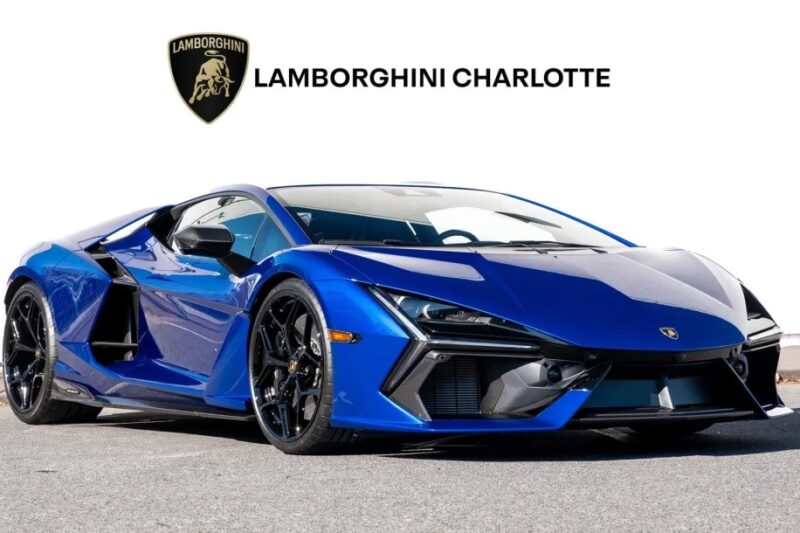 A blue 2024 Lamborghini parked on a gray surface with the "Lamborghini Charlotte" logo above it, showcasing the allure of a Lamborghini Revuelto.