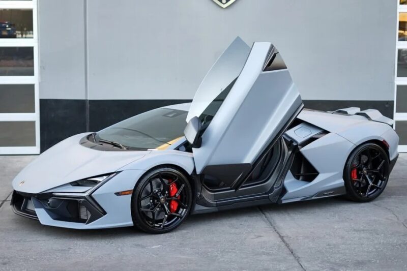 A 2024 Lamborghini with scissor doors open, black rims, and red brake calipers sits elegantly parked in front of a building.