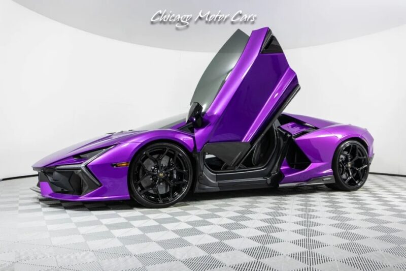 A stunning 2024 Lamborghini Revuelto is proudly displayed in the showroom, its purple finish gleaming against the checkered floor, with open scissor doors inviting you to step inside. This sleek sports car is now available for sale, offering a perfect blend of style and performance.