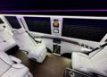 The 2024 Jet Sprinter by First Class Customs offers a luxurious limousine interior featuring four pristine white leather seats, a stylish small table, built-in screens, and subtle ambient lighting for an unparalleled travel experience.