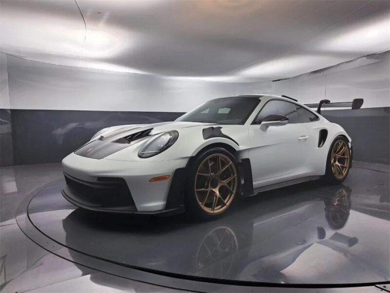 A Porsche 911 GT3 RS, the ultimate driver's car, with a large rear spoiler is displayed in a showroom.