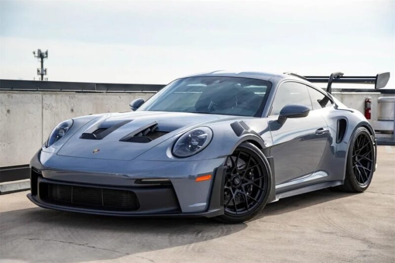 A sleek gray Porsche 911 with a large rear wing and black rims, parked on a rooftop, embodies the spirit of the ultimate driver's car.