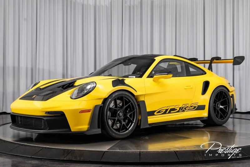 The ultimate yellow Porsche 911 GT3 RS, with black accents and a large rear spoiler, proudly showcases its "GT3 RS" branding on the side. It is displayed indoors on a rotating platform, epitomizing the pinnacle of a driver's car experience.