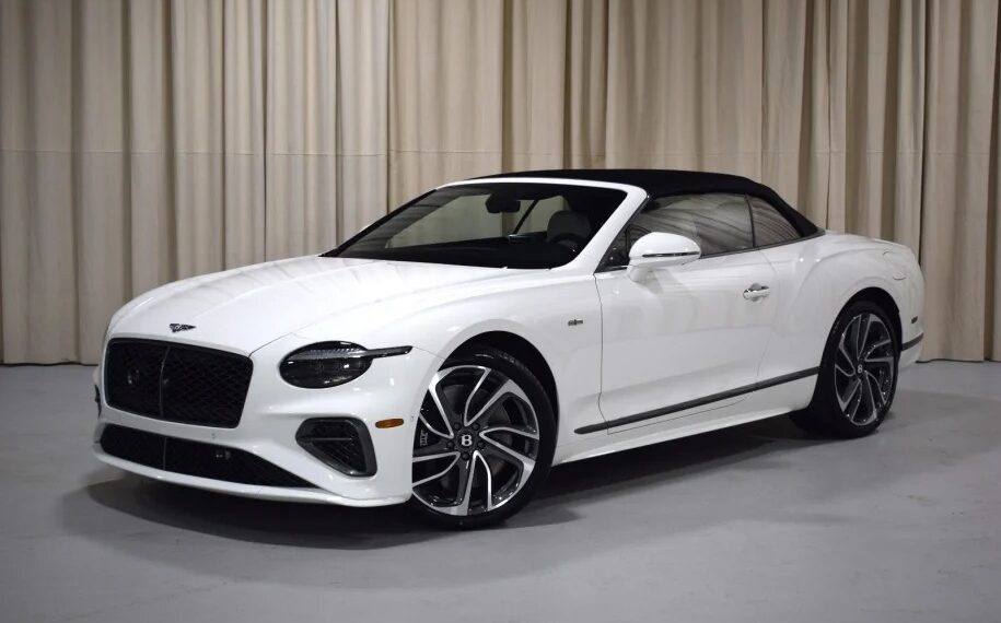 A luxurious Bentley Continental GTC convertible with a sleek black roof, elegantly parked indoors against a beige curtain backdrop.