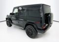 A sleek black electric Mercedes-Benz G-Wagon, 2025 model, elegantly parked in a pristine white studio, showcasing its rear side view.