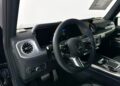 Interior view of a 2025 luxury electric Mercedes-Benz, featuring a G-Wagon-inspired steering wheel, digital dashboard, and sleek black trim.