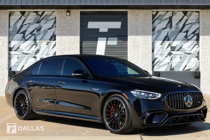 Sedan Mercedes-Benz hitam mewah diparkir dengan elegan di depan sebuah bangunan dengan jendela berpola indah, menampilkan desain klasik dan detail yang indah.