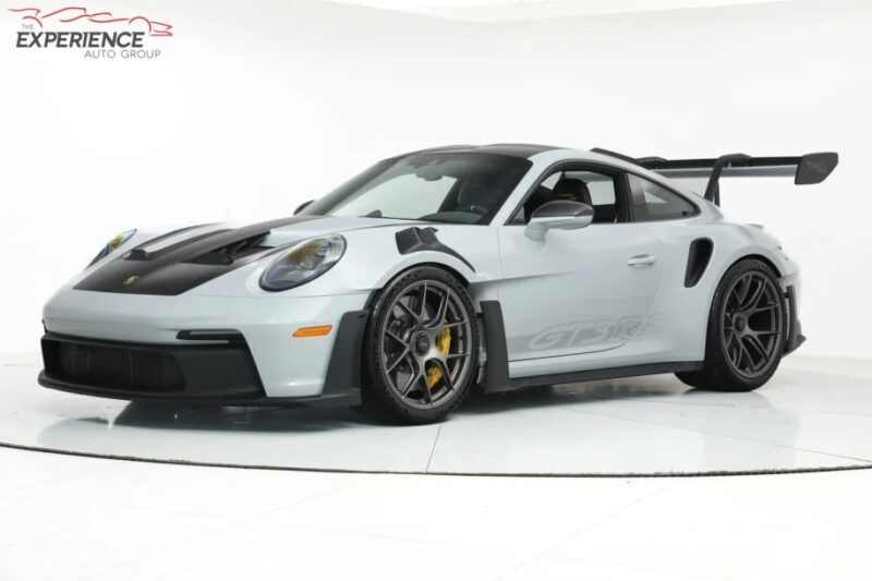 A silver Porsche 911 GT3 RS sports car with a large rear spoiler sits on display in a well-lit studio setting, embodying the essence of the ultimate driver's car.