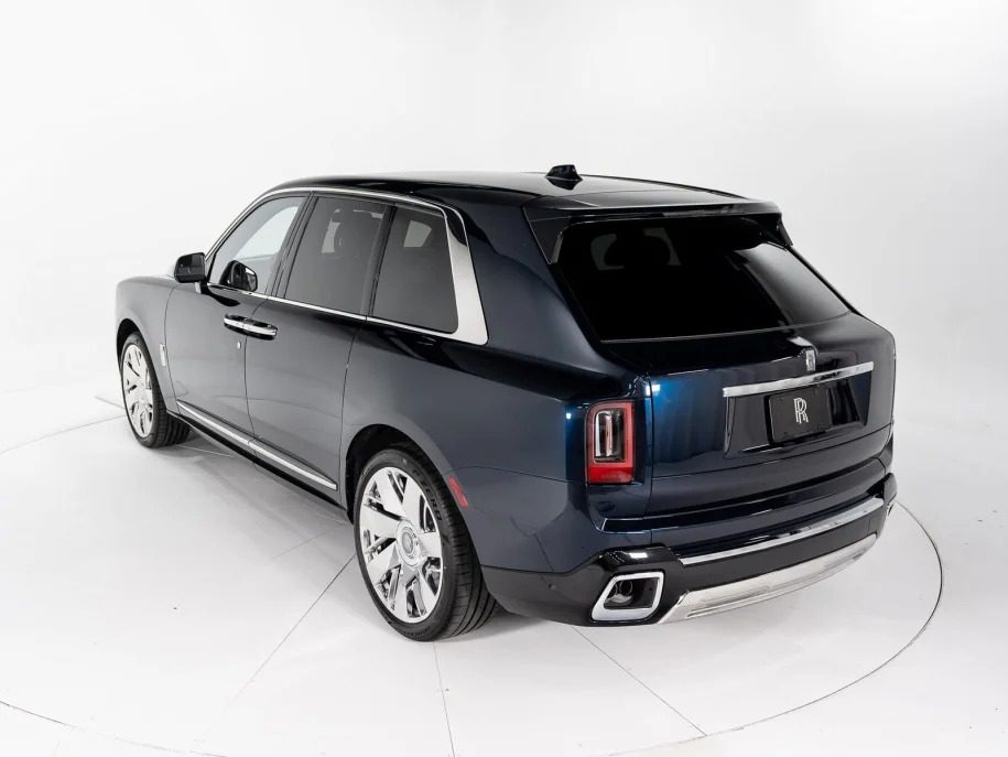 A dark blue Bentley Bentayga, the epitome of an Ultra-Luxe SUV, is parked in a pristine white studio, viewed from the rear side angle. The vehicle boasts polished wheels and a high-gloss finish.