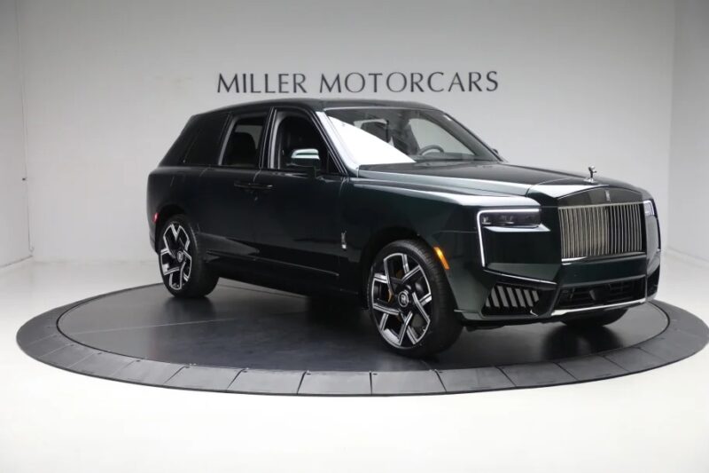 A dark green SUV with a powerful V12 engine sits on a rotating platform in the showroom, capturing attention at Miller Motorcars, where exotic cars define the experience.