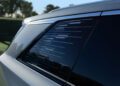 Close-up of a Cadillac window with horizontal line patterns. The background, framed by this luxury EV's sleek design, shows blurred greenery under a clear sky.