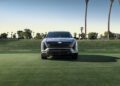 A silver Cadillac SUV is parked on a grassy field, with palm trees and a clear sky in the background, embodying the essence of luxury EV performance.