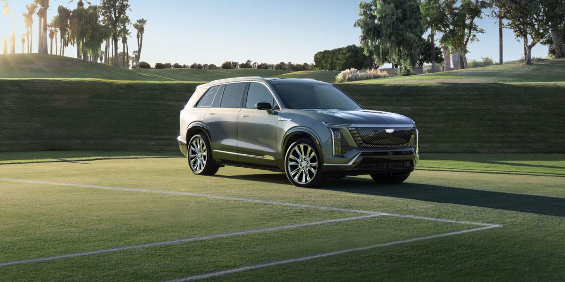 A silver Cadillac SUV is elegantly parked on a grassy field, framed by palm trees and a clear sky, showcasing the perfect blend of style and luxury.