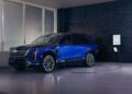 A Cadillac luxury EV, the sleek blue Vistiq SUV, charges effortlessly in the garage against a striking black brick wall backdrop.