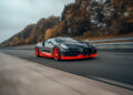 A sleek black and red Bugatti W16 Mistral speeds down the highway, its top speed unmatched as blurred autumn trees rush by in the background.