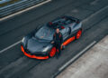 A person in racing gear stands beside a sleek black and orange Bugatti W16 Mistral on a racetrack, ready to challenge for the world record.