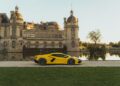 A yellow Lamborghini sports car is parked in front of an ornate, historical building with a moat in the background.