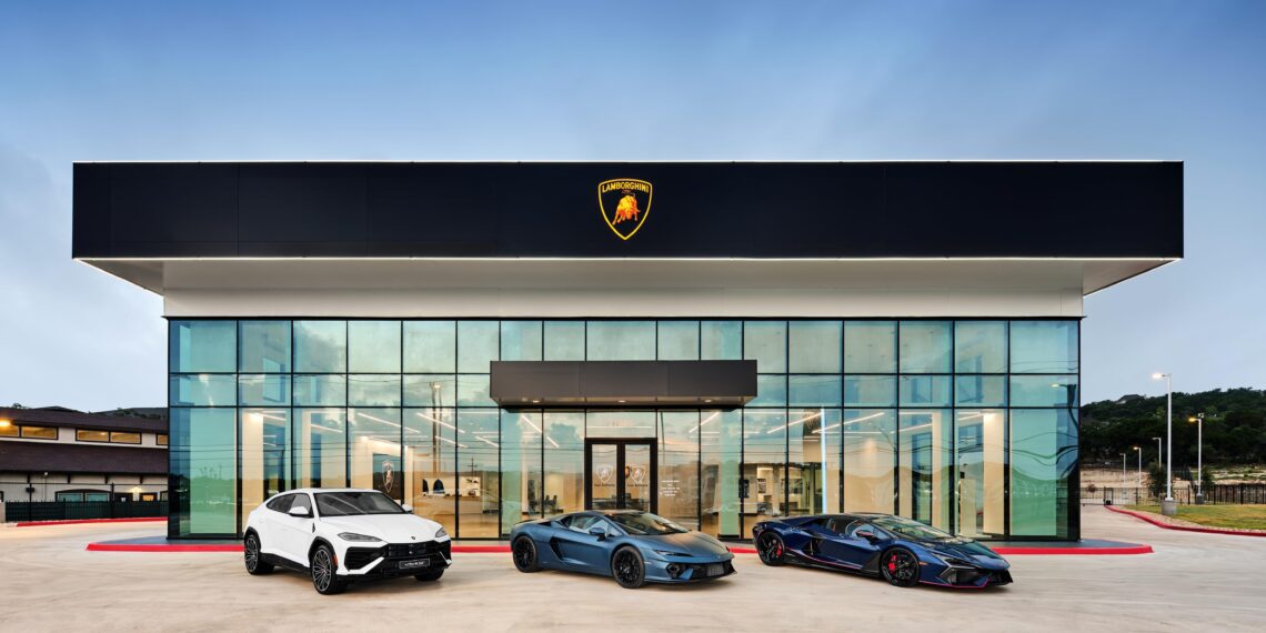 Three Lamborghini cars, part of the brand's record numbers, are parked in front of a modern dealership building with a glass facade under a clear blue sky.