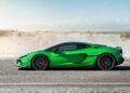 A striking green Lamborghini sports car is parked on a road, framed by sweeping sand dunes and a clear sky, setting the scene for record numbers of admirers to follow this new model debut.