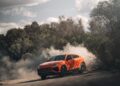 A sleek Lamborghini SUV makes a sharp turn on a dusty road surrounded by trees, creating a cloud of dust.