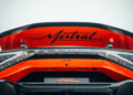 Close-up of the rear of a red Bugatti W16 Mistral, showcasing its iconic name on the spoiler and emblem below, with carbon fiber detailing that epitomizes luxury and speed, hinting at its world record-breaking capabilities.