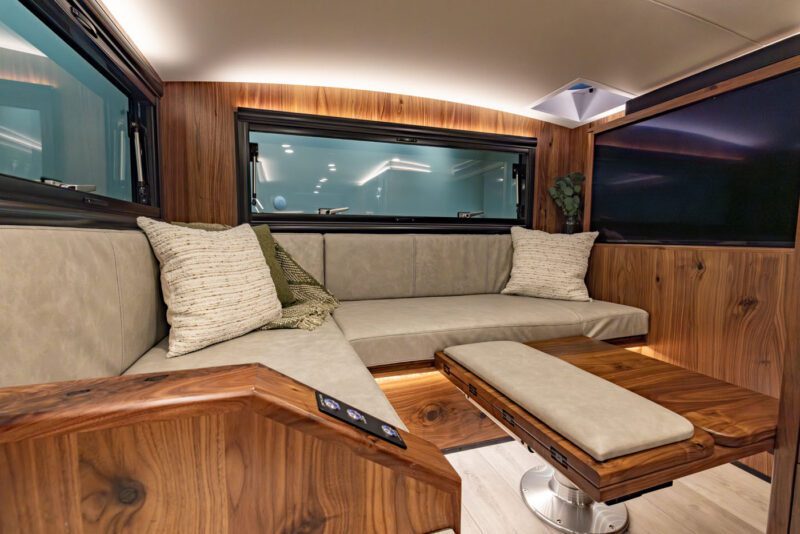 Experience the ultimate luxurious RV interior with elegant wood paneling, a U-shaped beige sofa, and a polished wooden table. Two plush pillows invite relaxation while a large window ensures breathtaking views on any expedition. Perfect for your next adventure in an EarthRoamer.