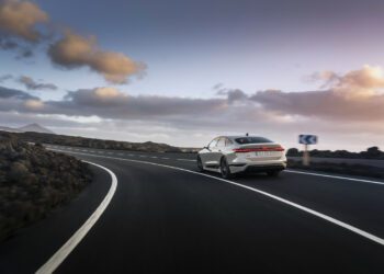 A sleek white car, reminiscent of a Lamborghini, navigates a curving road surrounded by rocky terrain under a partly cloudy sky, symbolizing the Audi Group's anticipated Q3 2024 success.