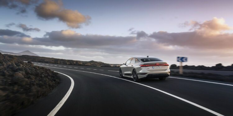 A sleek white car, reminiscent of a Lamborghini, navigates a curving road surrounded by rocky terrain under a partly cloudy sky, symbolizing the Audi Group's anticipated Q3 2024 success.