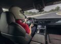 A driver in a helmet expertly steers an Audi RS Q8 on the racetrack, immersed in rigorous performance testing, surrounded by an array of controls and displays.