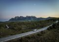 An Audi RS Q8 drives on a winding road amidst hilly terrain at dusk, its chassis developed to perfection, with a rugged mountain range in the background under a clear sky.