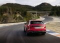 A red Audi RS Q8 is driving on a winding road with trees and a bridge in the background, showcasing its impressive performance.