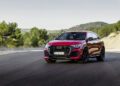 A red Audi RS Q8 SUV, a masterpiece by its chassis developers, is parked on a winding road surrounded by trees and hills.