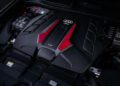 Close-up of an Audi RS Q8 engine cover with red and black accents, featuring a V8 label, showcasing the precision from its chassis developer.