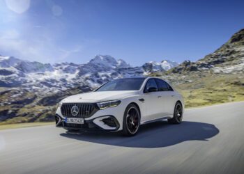 A sleek Mercedes-AMG E 53 hybrid car glides along a mountain road, framed by snowy peaks under a clear blue sky, offering a glimpse into the future of 2025 motoring.