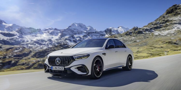 A sleek Mercedes-AMG E 53 hybrid car glides along a mountain road, framed by snowy peaks under a clear blue sky, offering a glimpse into the future of 2025 motoring.