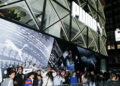 A crowd gathers outside the PUMA store, captivated by a large poster showcasing a thrilling PUMA Motorsport scene with the number 48, hinting at excitement akin to the A$AP Rocky Collection.