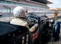 The driver, seated in a stunning Bentley Speed Six from the Continuation Series, prepares to enter the track at an empty race circuit, proudly showcasing the British flag on this vintage racing marvel.