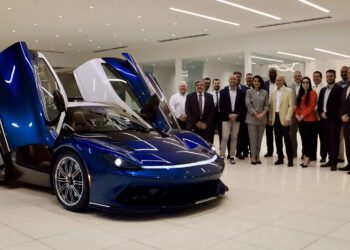 A group of people stands next to a blue sports car with its butterfly doors open inside a modern showroom.