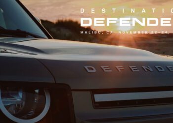 Close-up of a Land Rover Defender with "Destination Defender, Malibu, CA, November 22-24, 2024" text overlay against a stunning Malibu sunset backdrop.