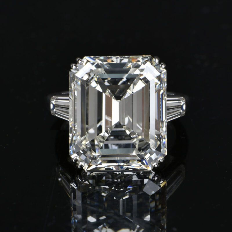 Emerald-cut diamond ring with rectangular facets, set in a simple metal band, showcased like an exquisite piece of jewelry on a reflective black surface.