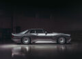 A sleek, silver Supercat sports car with a V12 manual transmission is parked indoors on a polished floor, viewed from the side against a dark background.