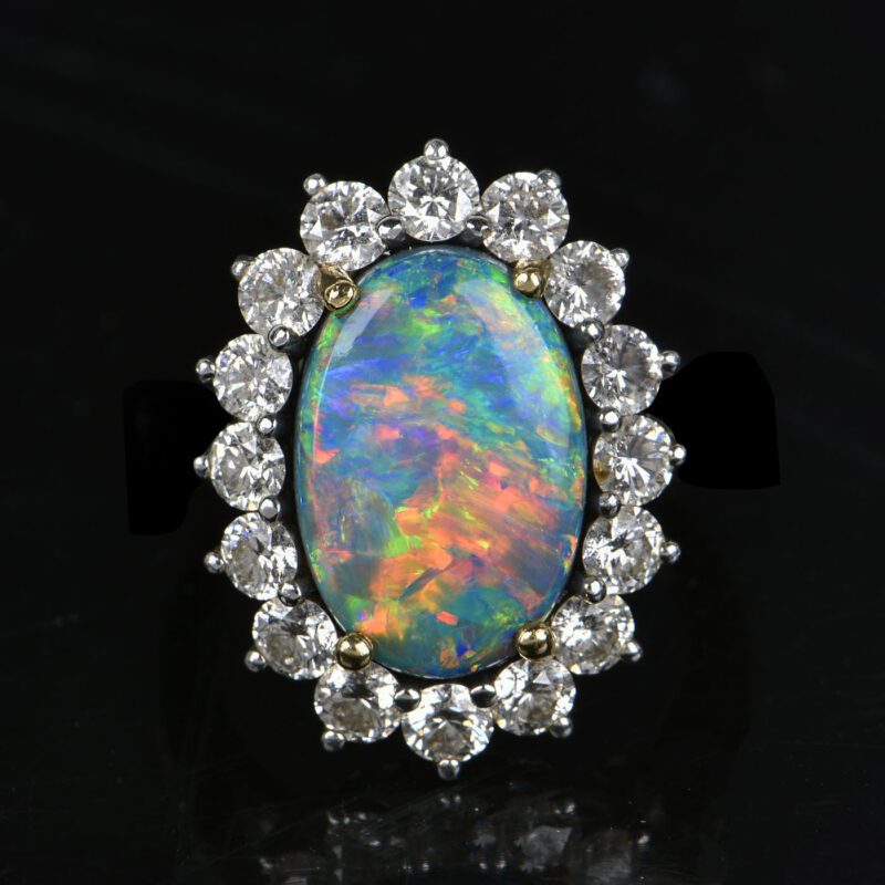 An opal ring featuring a large oval stone surrounded by small round diamonds is set in a stunning silver band, making it a standout piece of jewelry that could easily become the highlight of any auction.