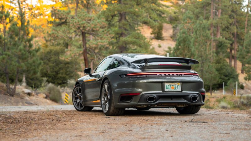 A gray sports car parked on a forest road with trees in the background.