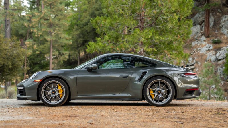 A gray sports car parked on a dirt road, surrounded by trees and greenery.