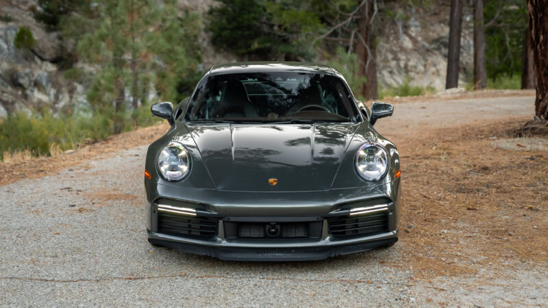 Front view of a dark gray Porsche sports car parked on a forest road.