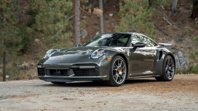 A sleek grey sports car parked on a gravel path, surrounded by trees.