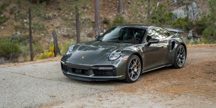 A gray sports car parked on a gravel path in a wooded area.