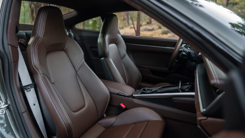 Interior of a car featuring brown leather seats, a sleek dashboard, and minimalistic controls, set in a forested background seen through the windows.