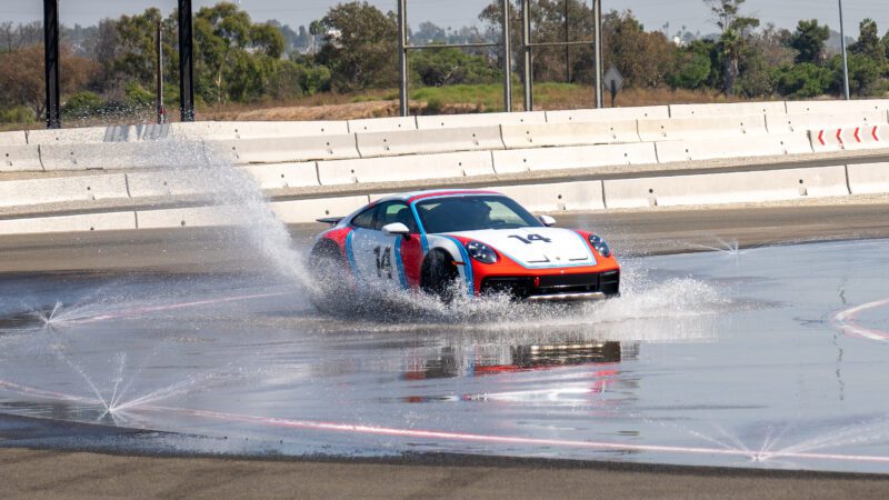 A sports car with the number 14 on it splashes through water on a wet racetrack.